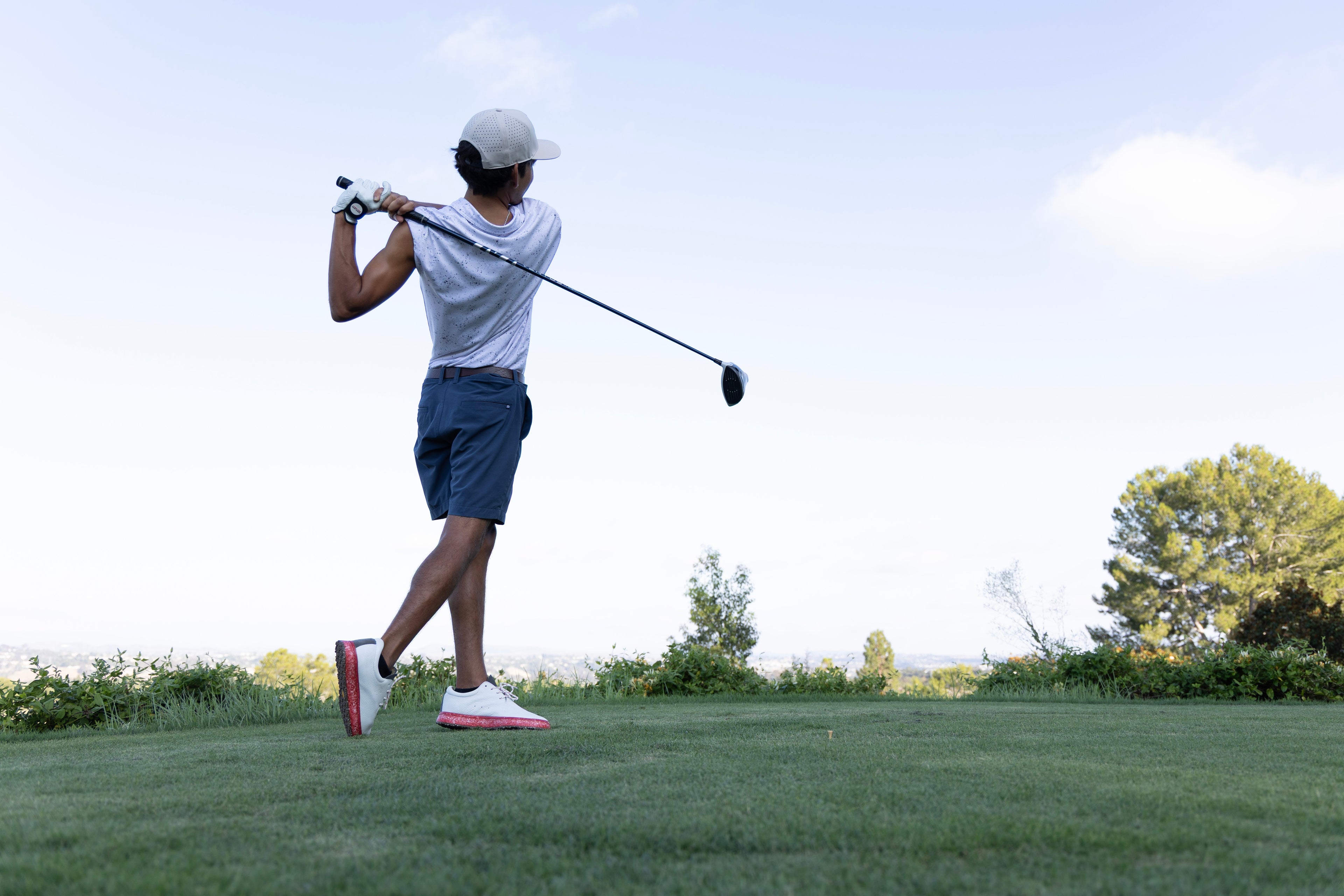 Young golfer hitting a tee shot in red and white spikeless golf shoes made with premium white leather and recycled performance foam midsole and insole components 