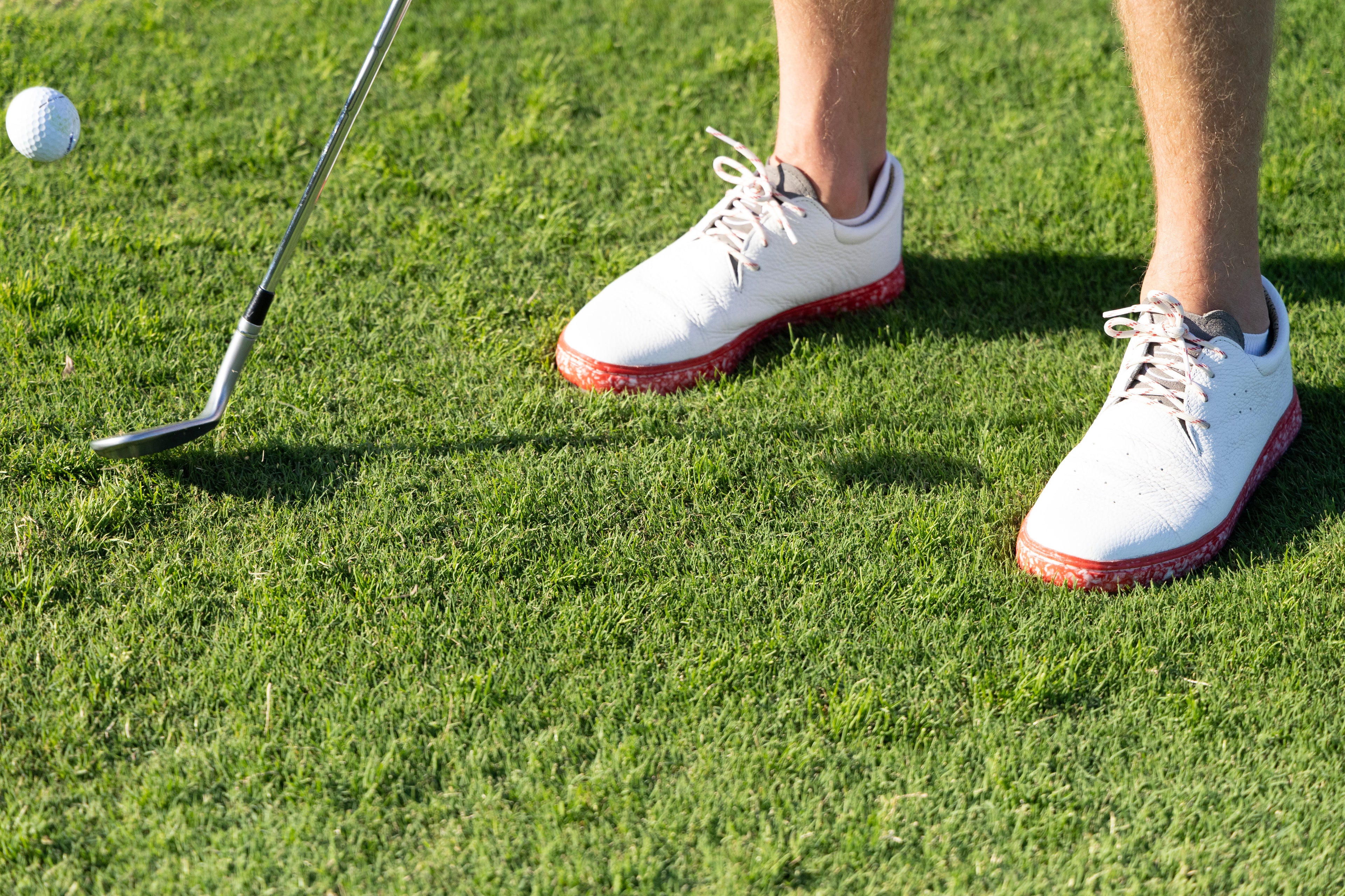 Golfer hitting a chip in premium white leather golf shoe with Blumaka recycled foam components