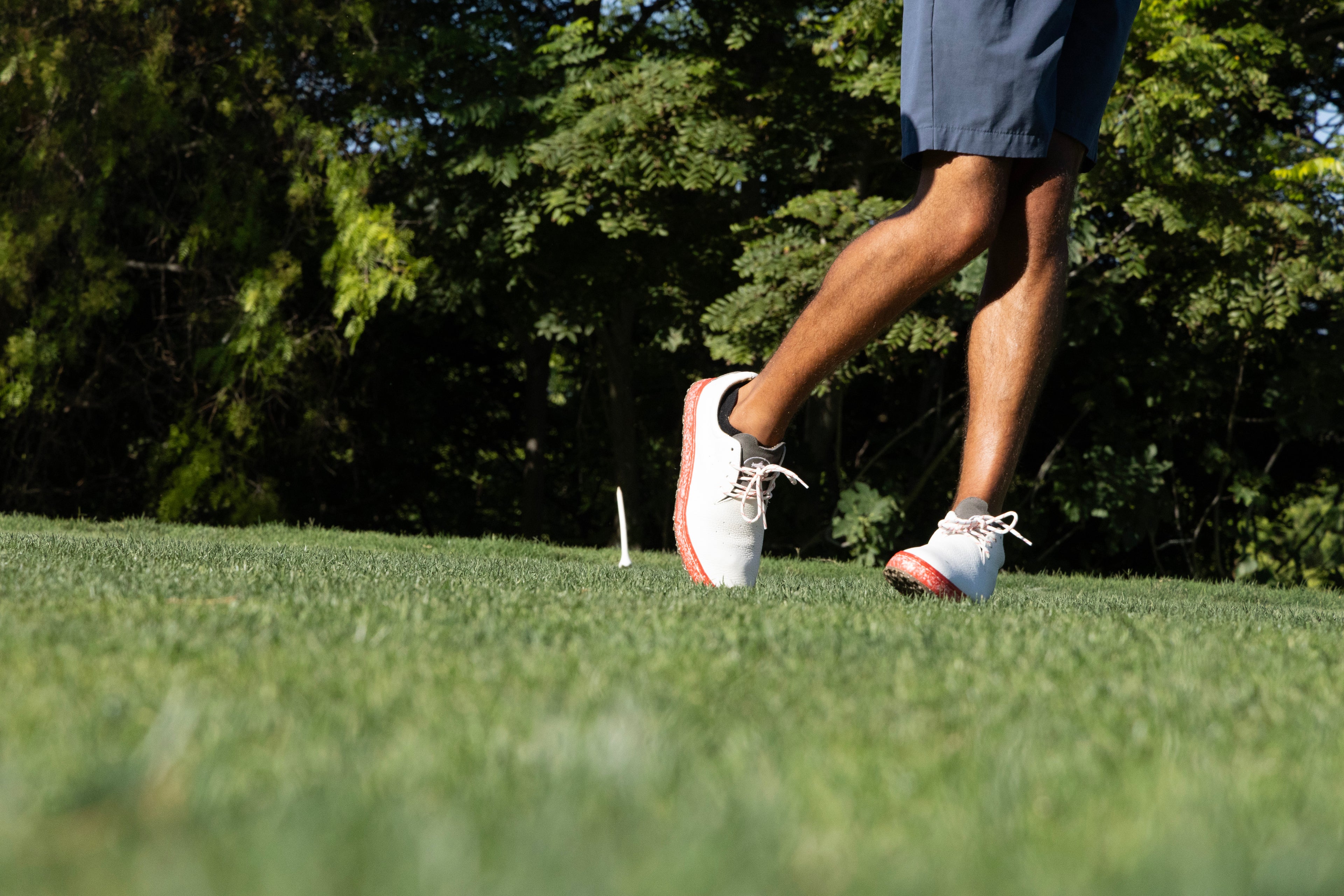 Golfer hitting a tee shot in premium white leather golf shoes with recycled performance foam components from BLUMAKA