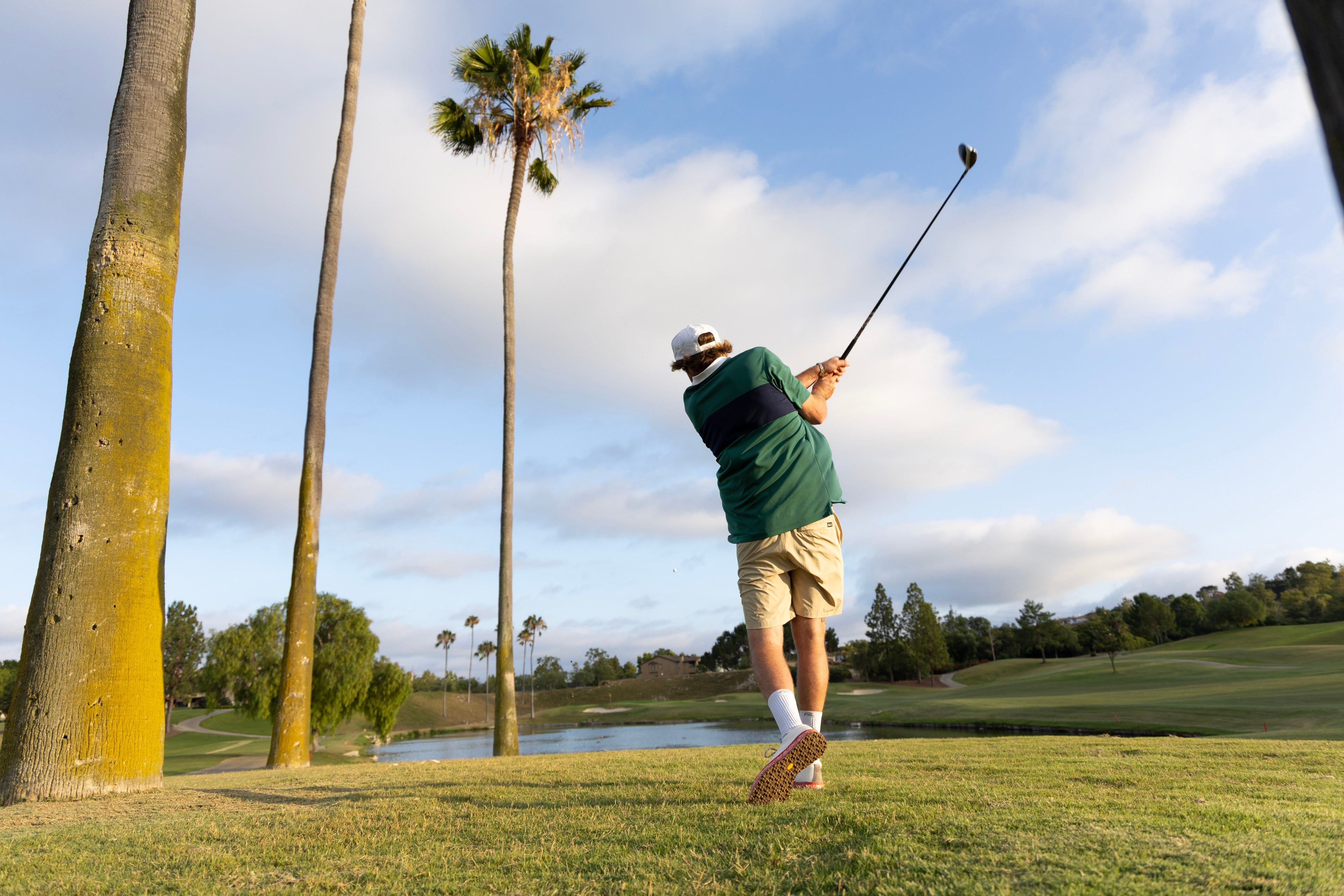 Golfer hitting a fairway wood around palm trees in premium white leather golf shoe with Blumaka recycled foam components