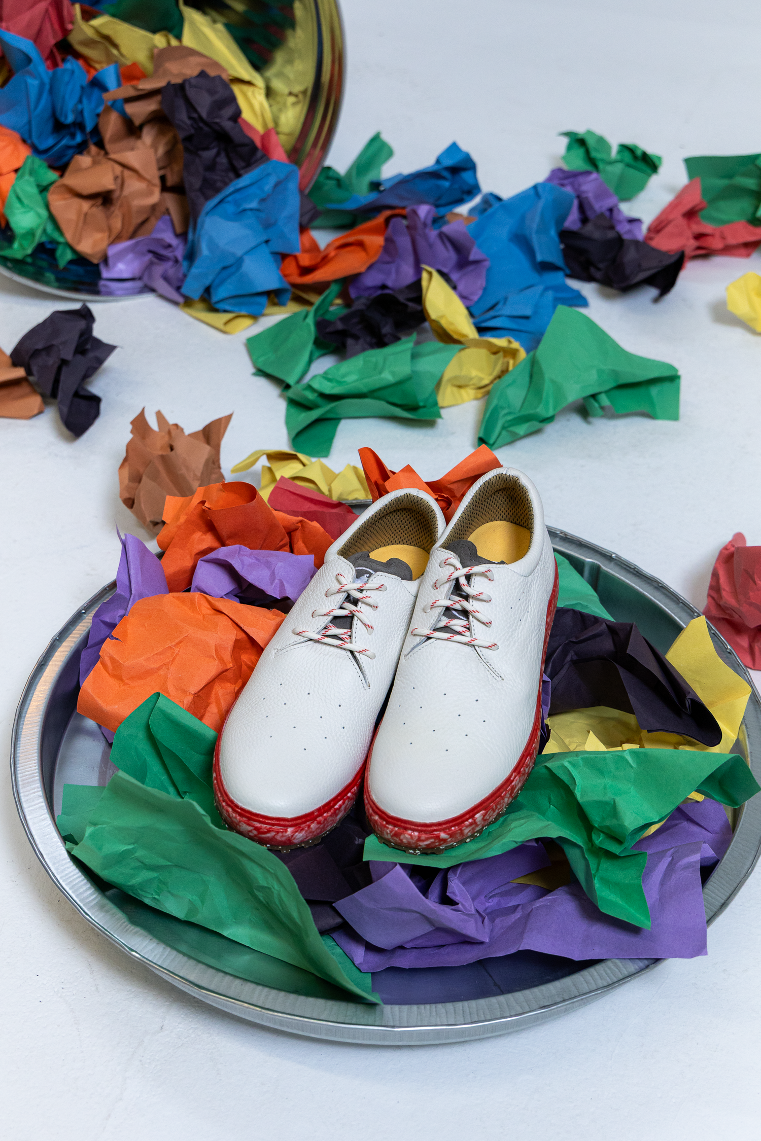 A pair of red and white premium leather golf shoes sitting on crumpled paper representing trash because their midsole and insole components are made with up to 85% recycled foam